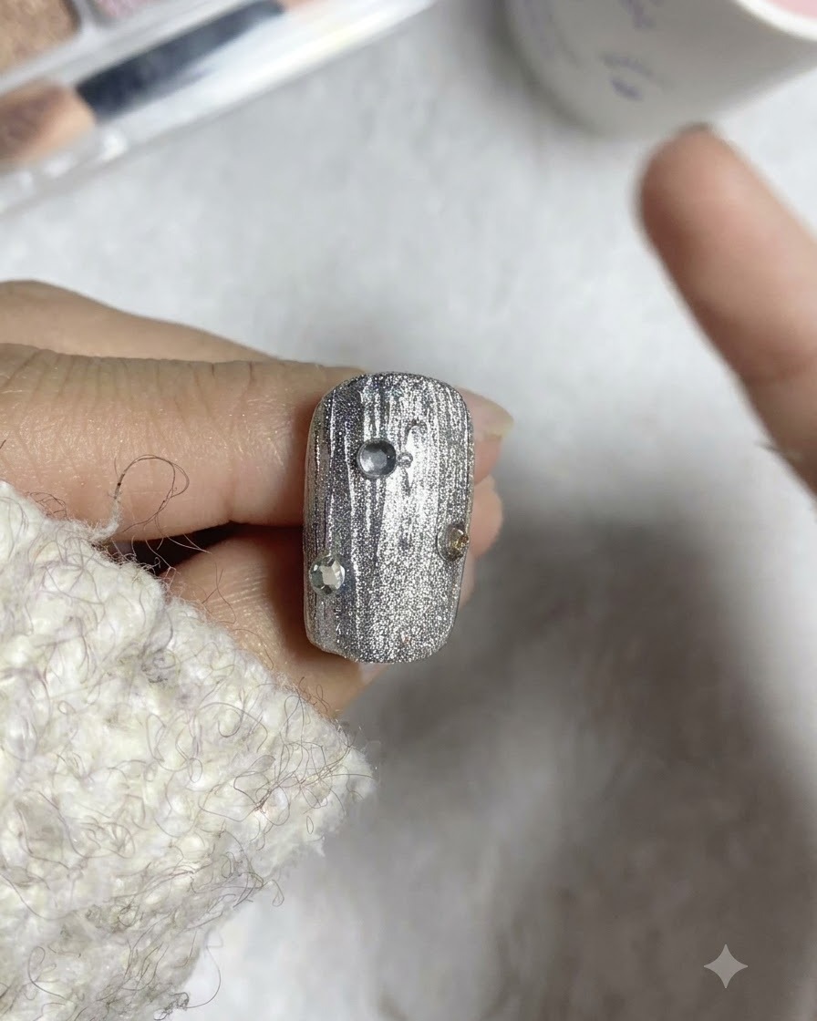 Un pinceau liner plaçant de petites billes dacier autour de strass sur un ongle texturé.