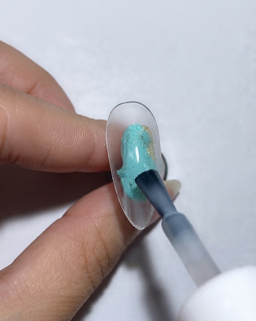 Un pinceau appliquant une base en gel protéiné sur un ongle daffichage transparent.