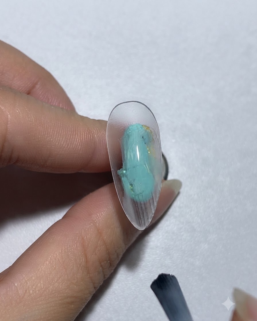 Un pinceau appliquant du gel de peinture bleu-vert sur un ongle.