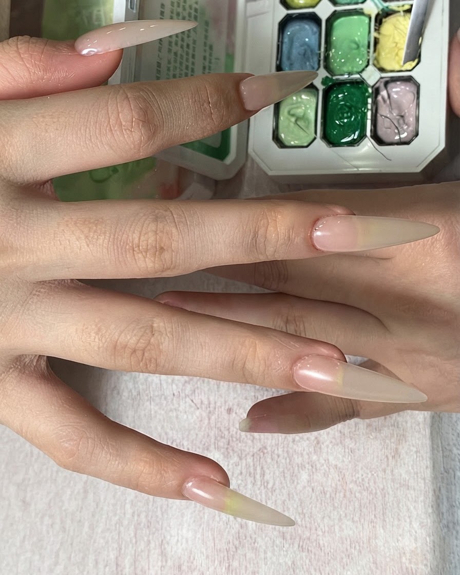Une main tenant une éponge cosmétique, tapotant la couleur jaune sur le bout dun long ongle en amande.