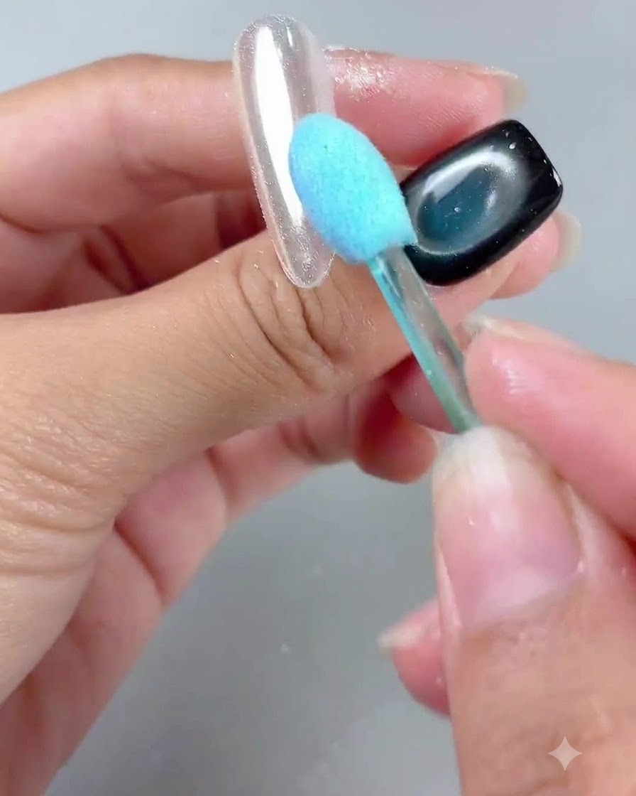 Un pinceau à poignée bleue balayant délicatement la poudre dun ongle au fini miroir brillant.