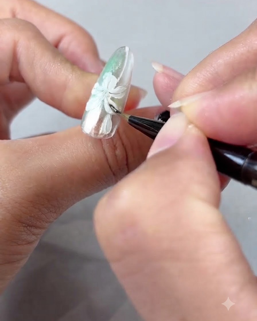 Un pinceau à ongles estompant délicatement lombrage en gel ambré sur les pétales de lys peints en blanc.