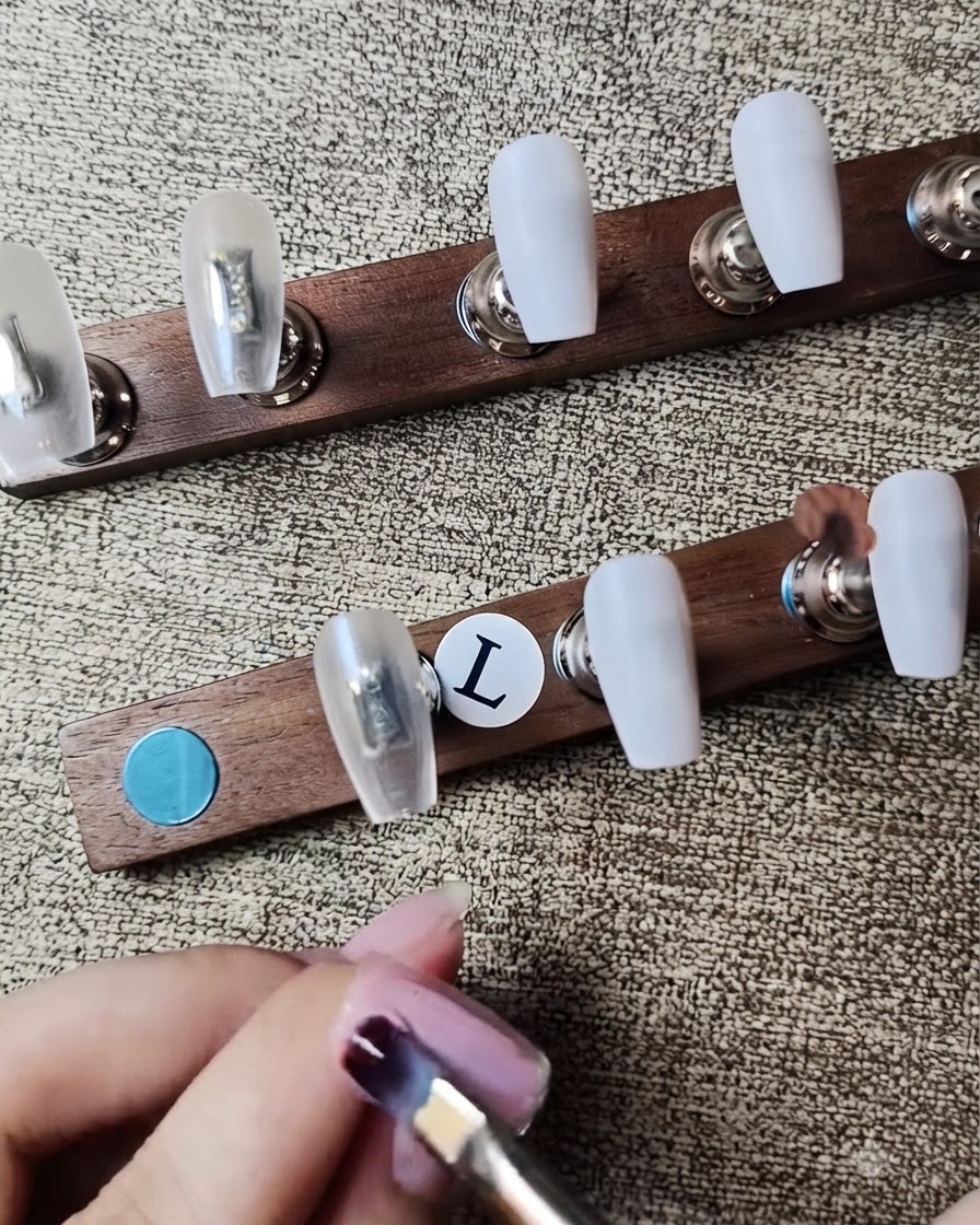 Un pinceau à gel plat appliquant un vernis gel rose nude diaphane sur un faux-ongle.