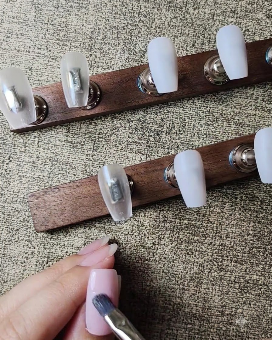 Un pinceau à gel plat appliquant une deuxième couche de vernis gel rose nude transparent sur longle.