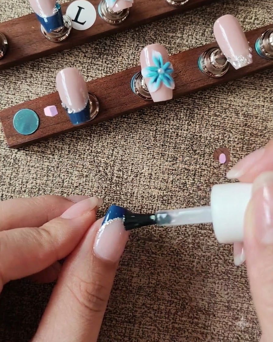 Un pinceau appliquant un top coat sur la surface de longle tout en contournant un accent floral 3D.