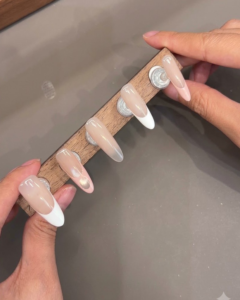 Plusieurs faux ongles montés sur un support en bois affichant des couches de top coat brillantes.