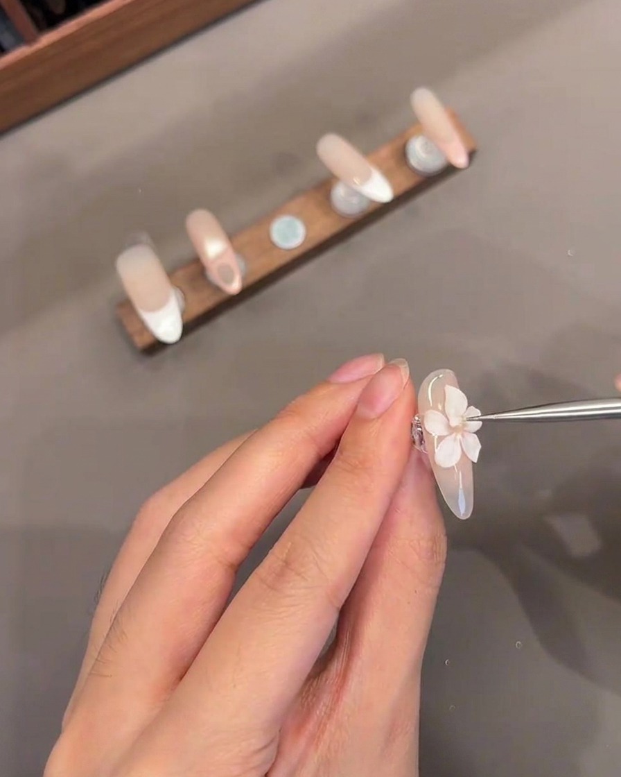 Un gros plan dun outil fin ajoutant un petit centre en gel blanc à une fleur 3D sculptée sur un onglet.