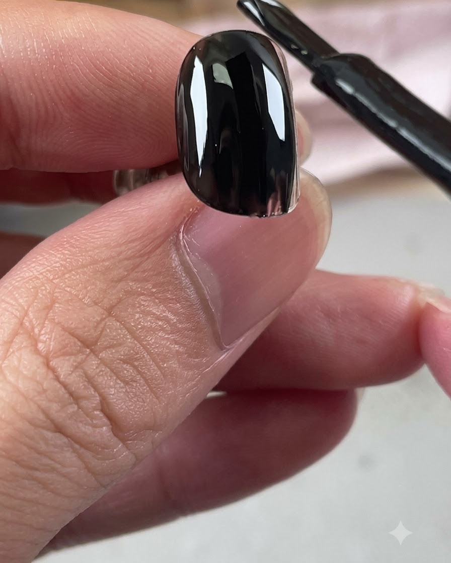 Un pinceau de flacon de vernis gel noir appliquant une couche brillante de base noire sur un ongle.