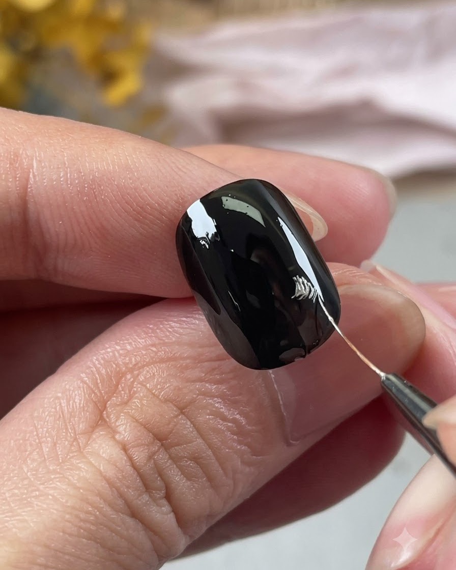 Une vue rapprochée dune main utilisant un pinceau de nail art fin pour dessiner des contours de pétales argentés sur un ongle noir.