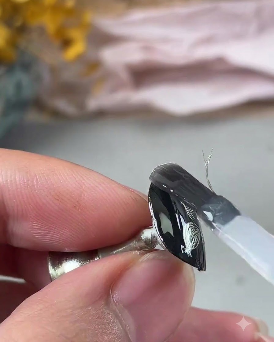 Un pinceau appliquant une couche de gel de renforcement transparent sur le design de nail art métallique texturé.