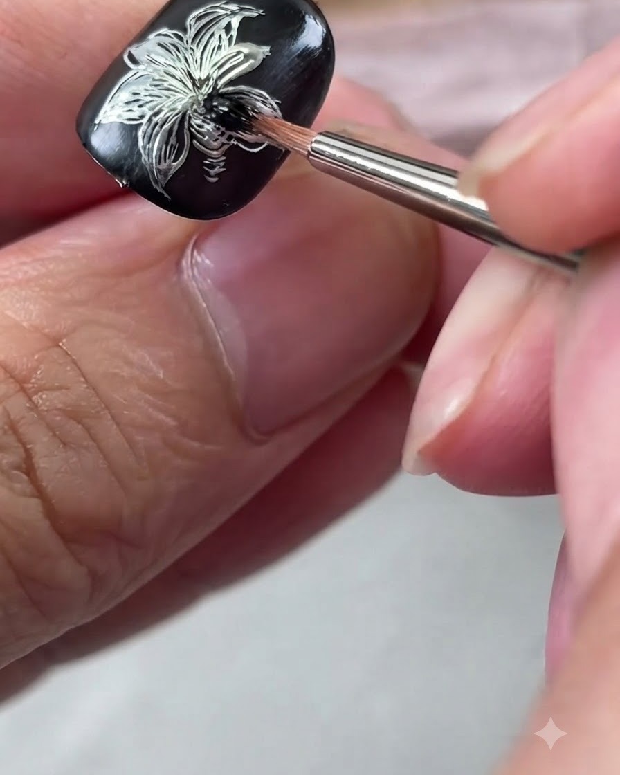 Un pinceau de détail estompant du vernis gel noir au centre dun design dongle de lys argenté métallique.