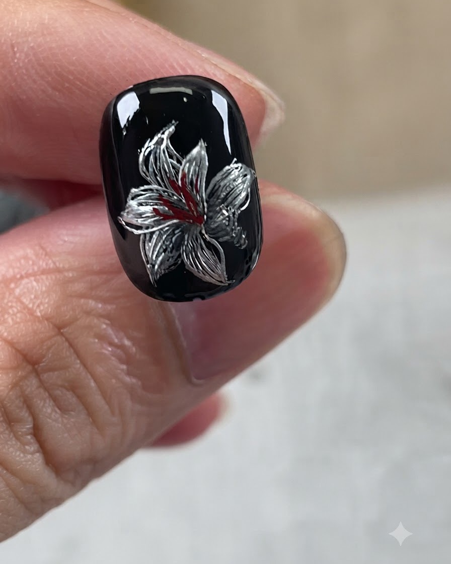 Un design de nail art de lys métallique achevé présentant une base noire, des pétales argentés, des accents blancs et des détails rouges au centre.