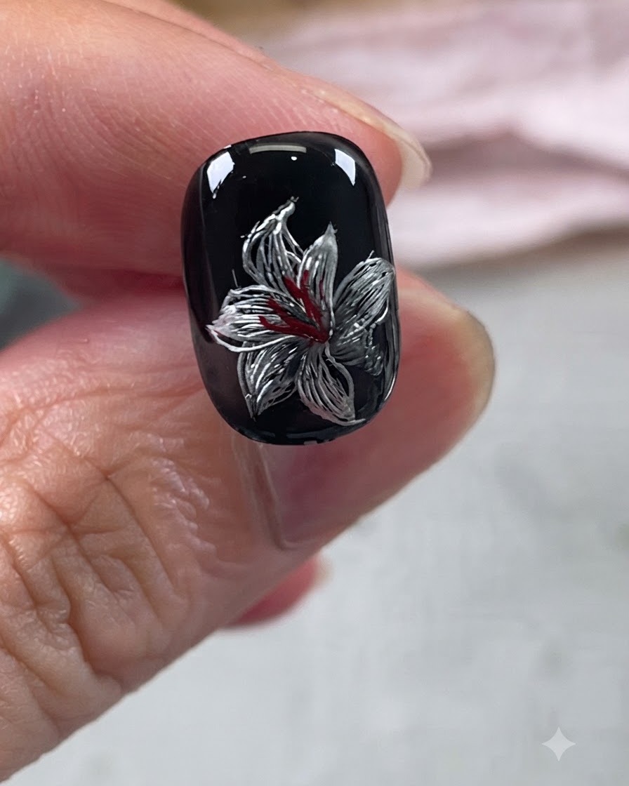 Un design de nail art de lys métallique achevé sur une base noire avec des détails rouges et argentés sous un top coat brillant.