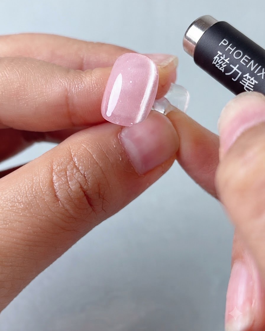 Un outil stylo magnétique survolant un ongle en gel œil-de-chat rose pour façonner la bande lumineuse.