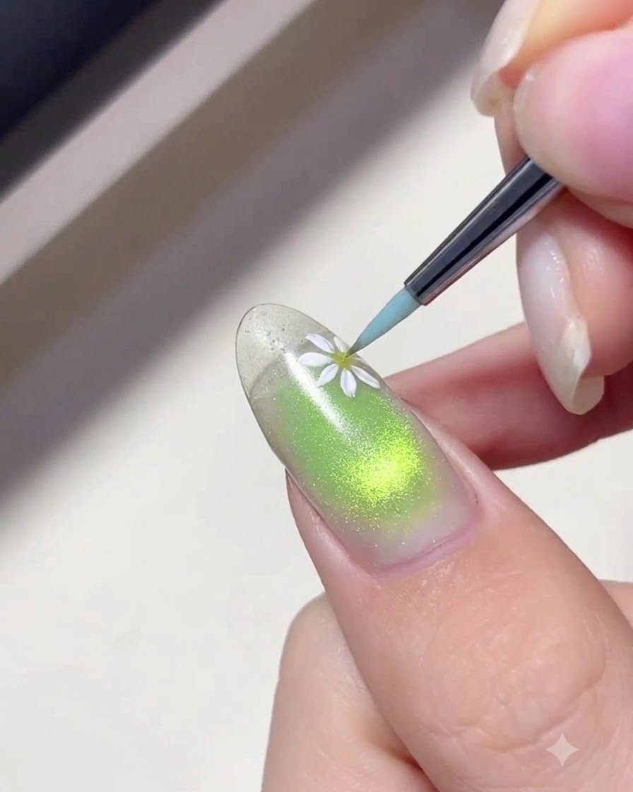 Un pinceau fin de nail art appliquant du gel blanc pour peindre de délicatiques pétales de marguerite sur un ongle au dégradé vert.