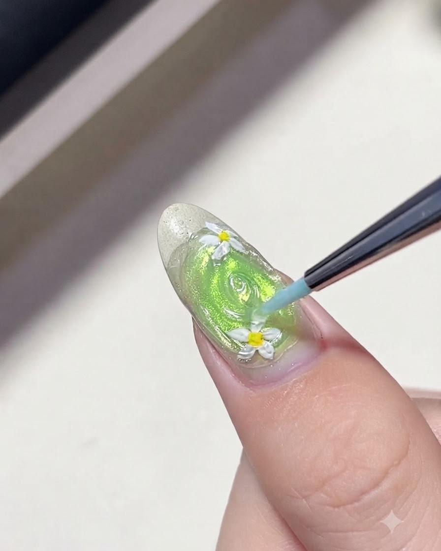 Un pinceau liner fin dessinant des cercles concentriques en gel transparent autour des marguerites sur un ongle vert pour créer des vagues deau.