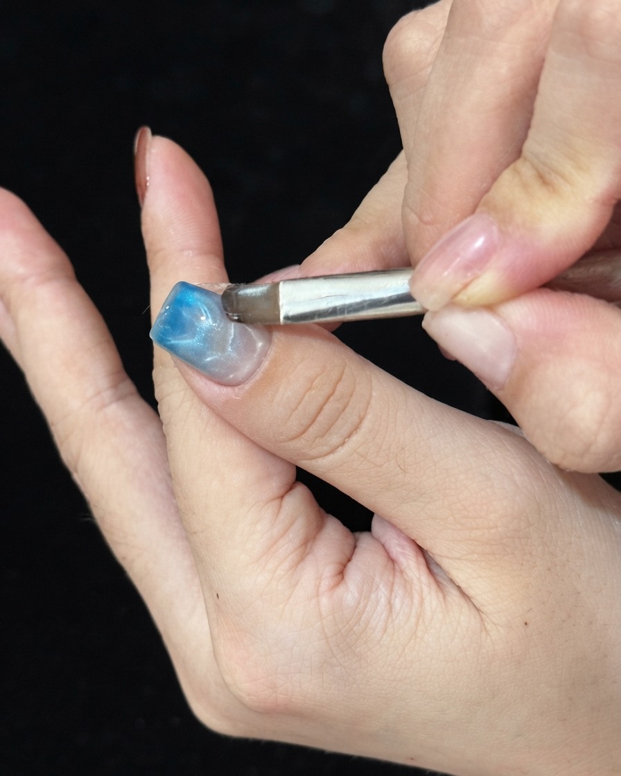 Un pinceau appliquant du gel verrier bleu sur le bout dun ongle manucuré pour créer un dégradé ombré.