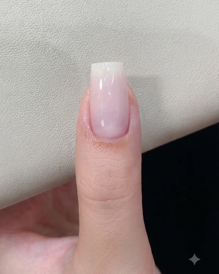 Un onglet avec une base de gel blanc laiteux catalysée reposant sous une lampe à ongles.