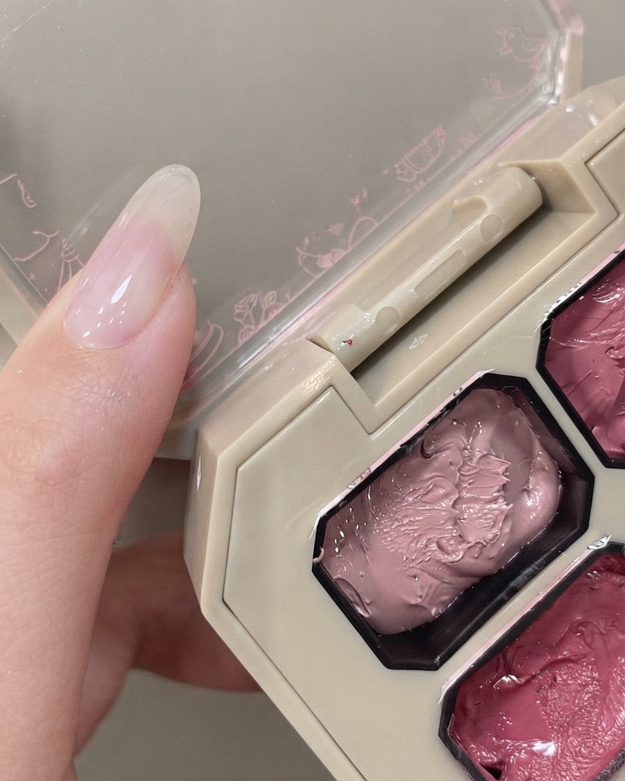 Un applicateur éponge survolant une palette de pigments roses à côté dune main avec un ongle naturel.