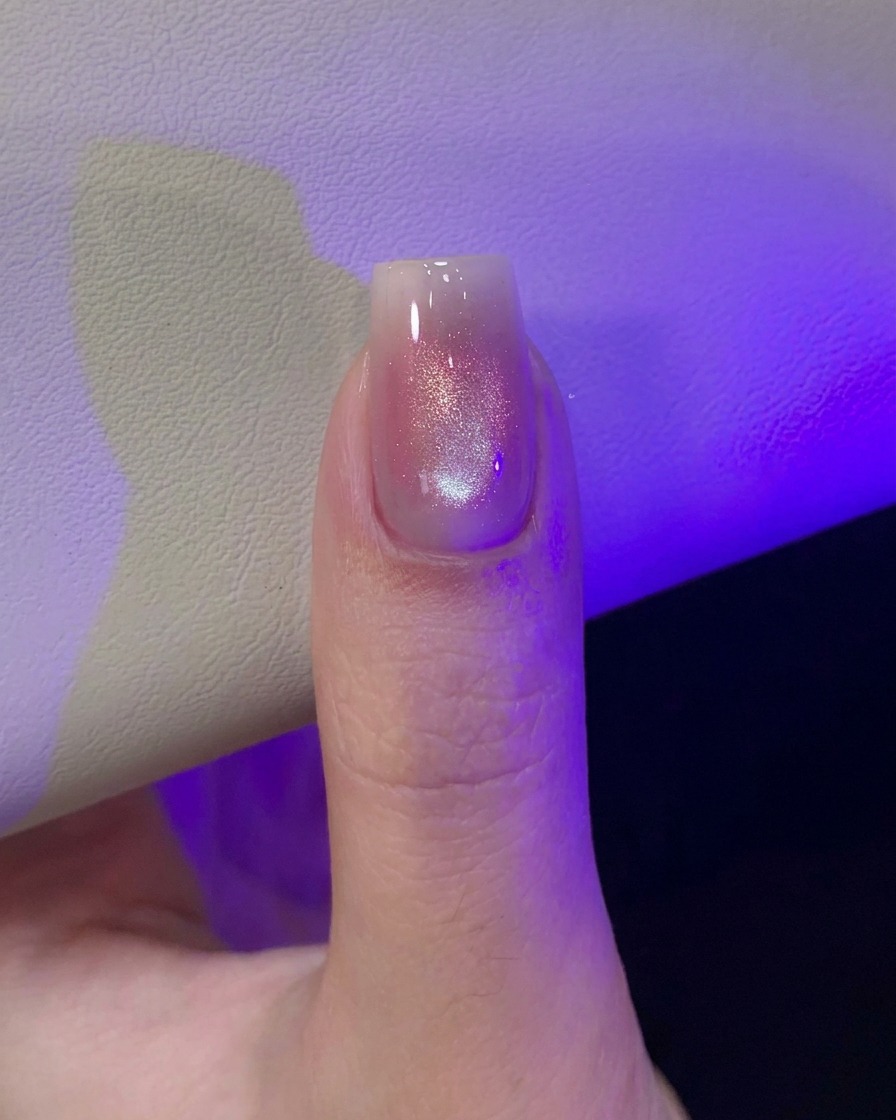 Un pouce sous la lumière violette dune lampe UV/LED catalysant le design dongle œil-de-chat fraîchement magnétisé.