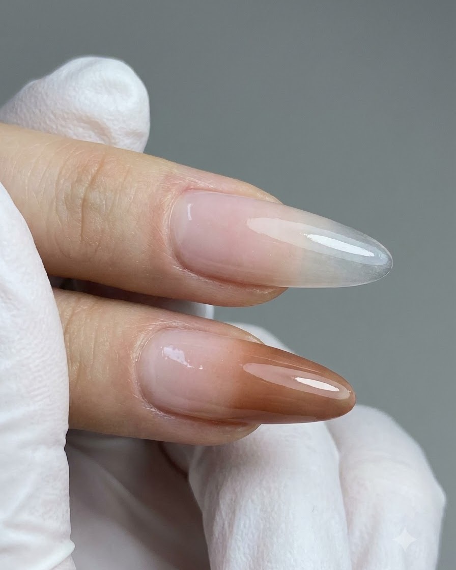 Un pinceau de détail appliquant du gel nude pêche sur la moitié inférieure dun faux ongle transparent allongé.