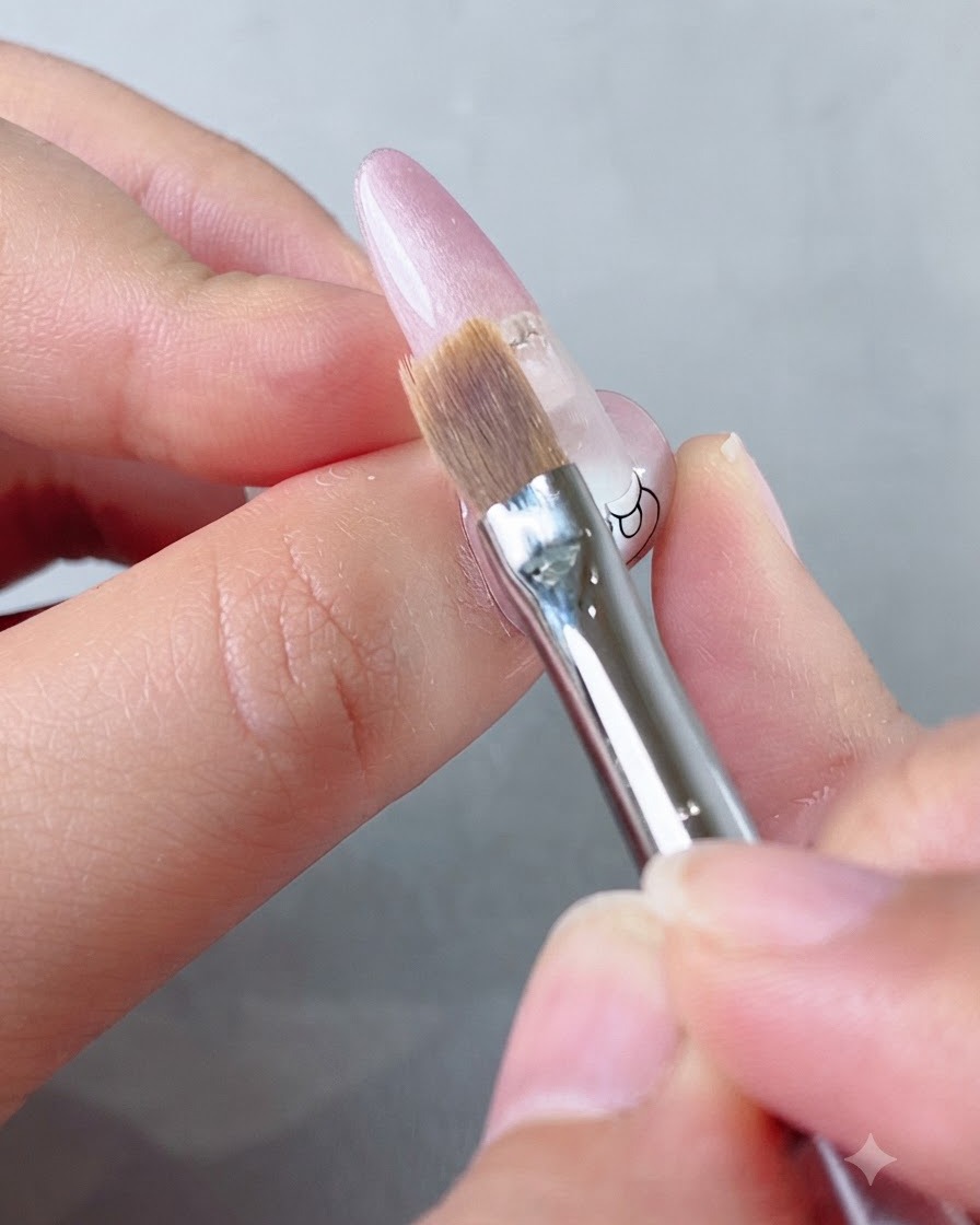 Gros plan dun pinceau plat et doux étirant doucement du vernis gel rose vers le bas sur un ongle.