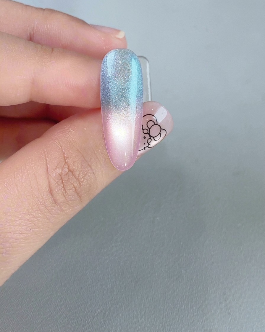 Un ongle terminé montrant un reflet œil de chat brillant et lumineux sur un dégradé rose et bleu.