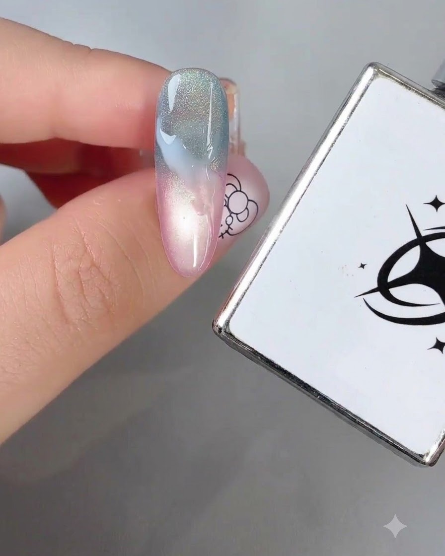 Un pinceau fin lissant de la peinture gel blanche sur un fond ombré bleu et rose pastel.