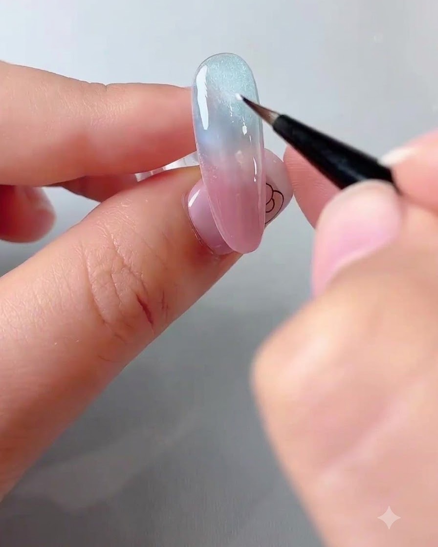 Une prothésiste ongulaire utilisant un pinceau fin pour déposer une touche de gel blanc sur un ongle dégradé bleu et rose.