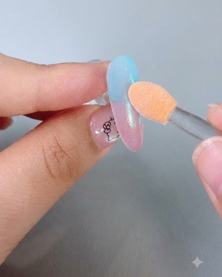 Un applicateur de fard à paupières éponge orange frottant de la poudre scintillante sur un ongle dégradé brillant.