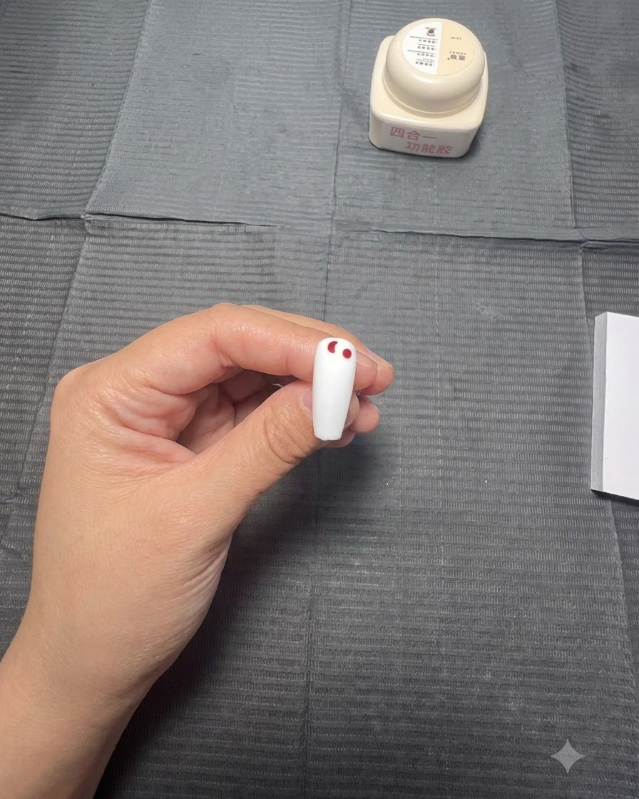 Une main utilisant un stylet pour placer une ligne décroissante de points rouges sur un ongle blanc.