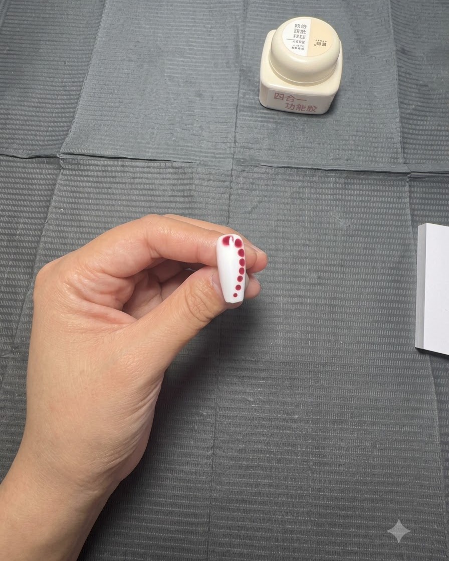 Un ongle avec une ligne de points rouges décroissants laissée au repos alors que la couleur commence à sétendre légèrement dans la base de gel humide.