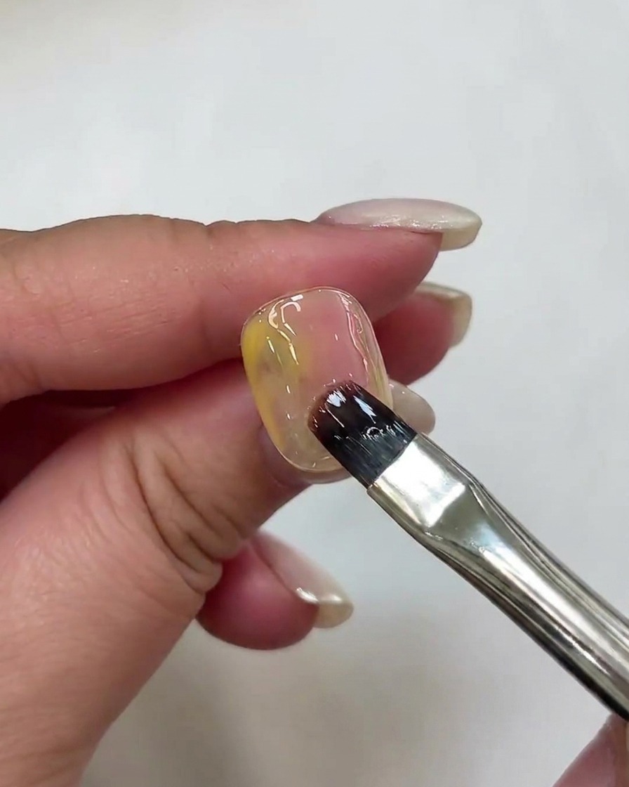 Un pinceau à ongle appliquant une nuance plus profonde de gel rose sur la surface de longle.