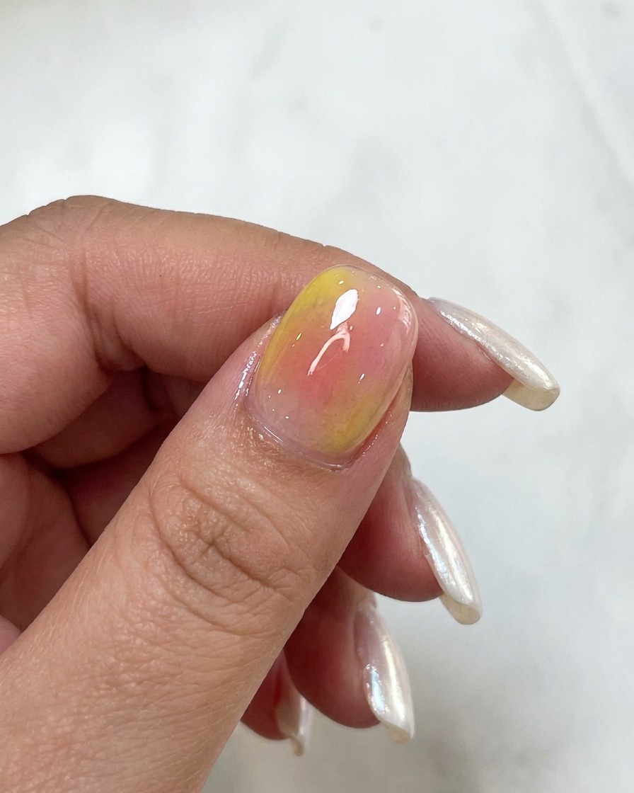 Une vue rapprochée dun ongle montrant des tons aquarelle rose et jaune superposés.