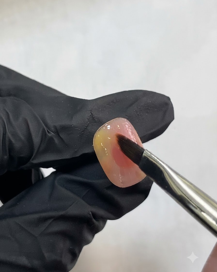 Un pinceau à ongle appliquant délicatement un petit trait de gel blanc translucide sur un ongle rose aquarelle.