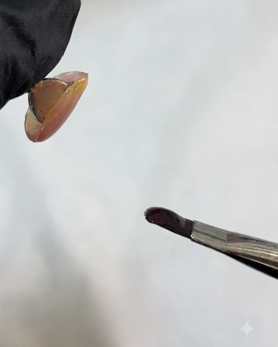 Un pinceau à ongle tenant du gel foncé près de la surface dun ongle.