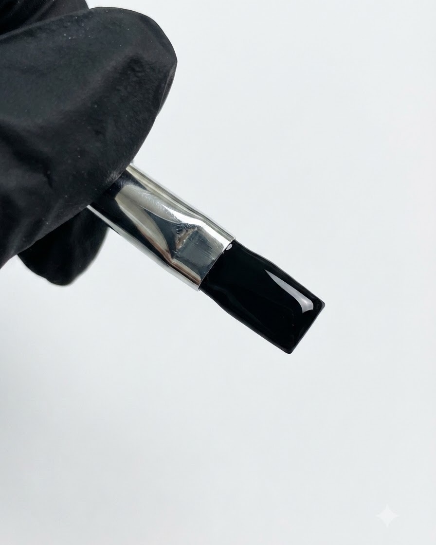 Une main gantée tenant un pinceau chargé de gel noir.