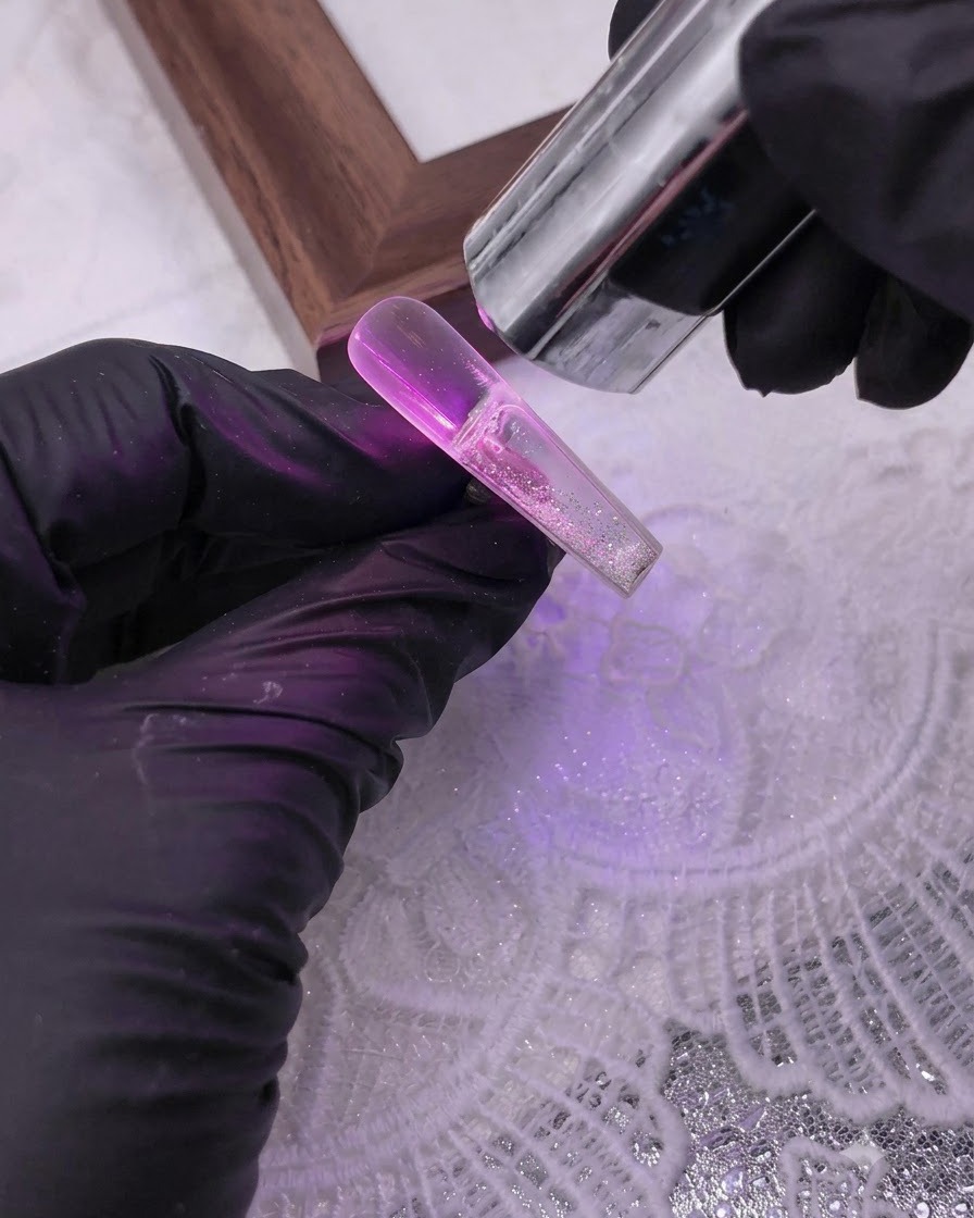 Une main gantée utilisant une seringue pour injecter un liquide transparent dans une capsule dongle artificielle creuse remplie de paillettes sous une lampe UV.