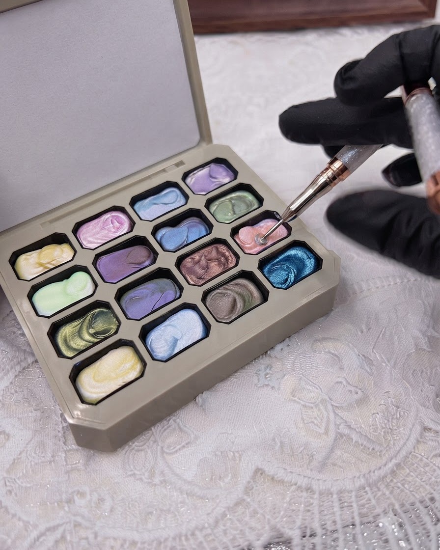 Un pinceau fin pour nail art prélevant du gel rose solide sur une palette multicolore de style maquillage.