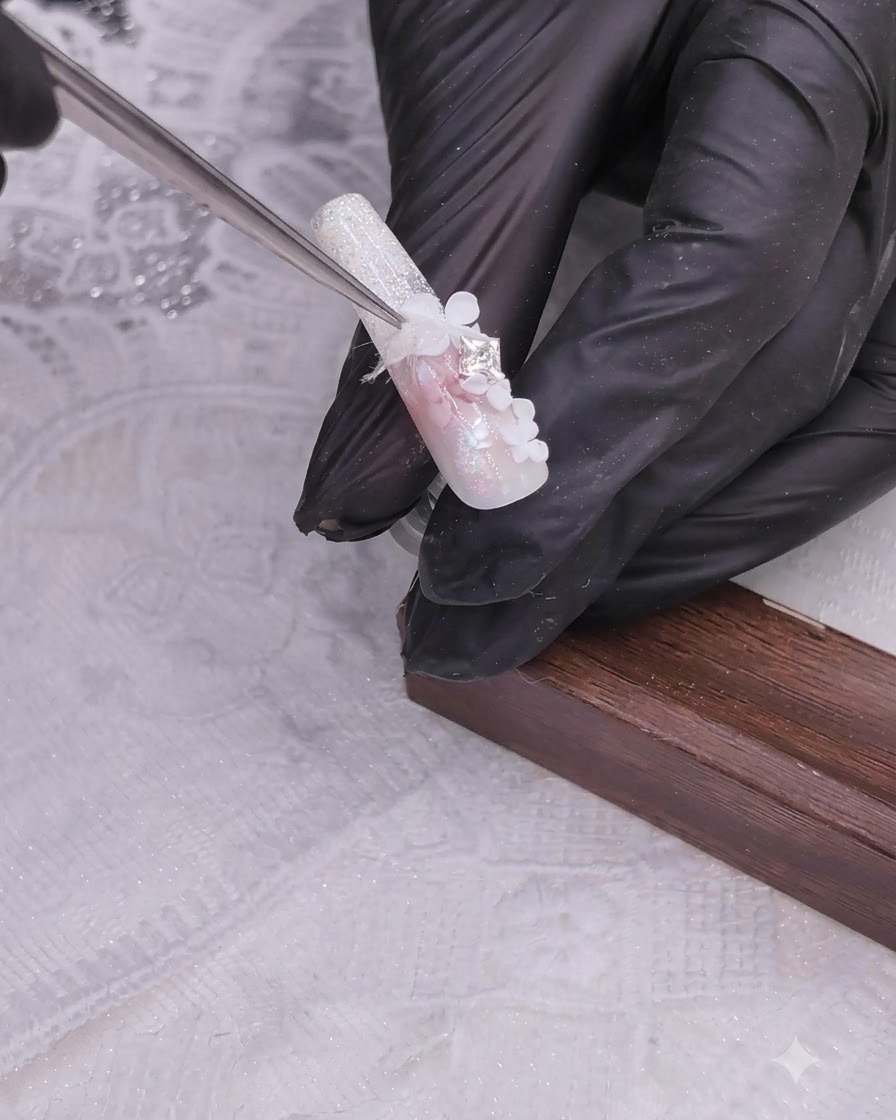 Une main gantée tenant une pince pour poser un strass scintillant sur un délicat bouquet floral en nail art.