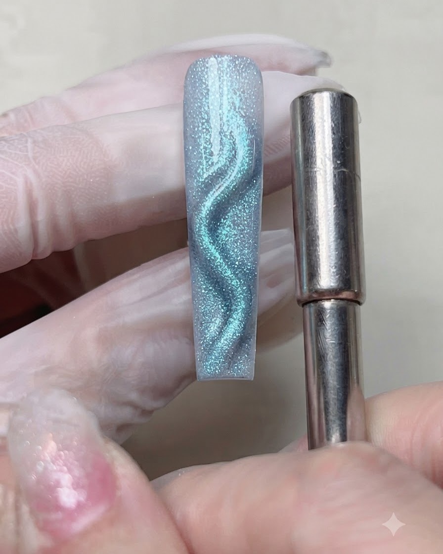 Un aimant cylindrique tenu près dun ongle avec du gel magnétique bleu humide, déplaçant le reflet en une ligne incurvée.