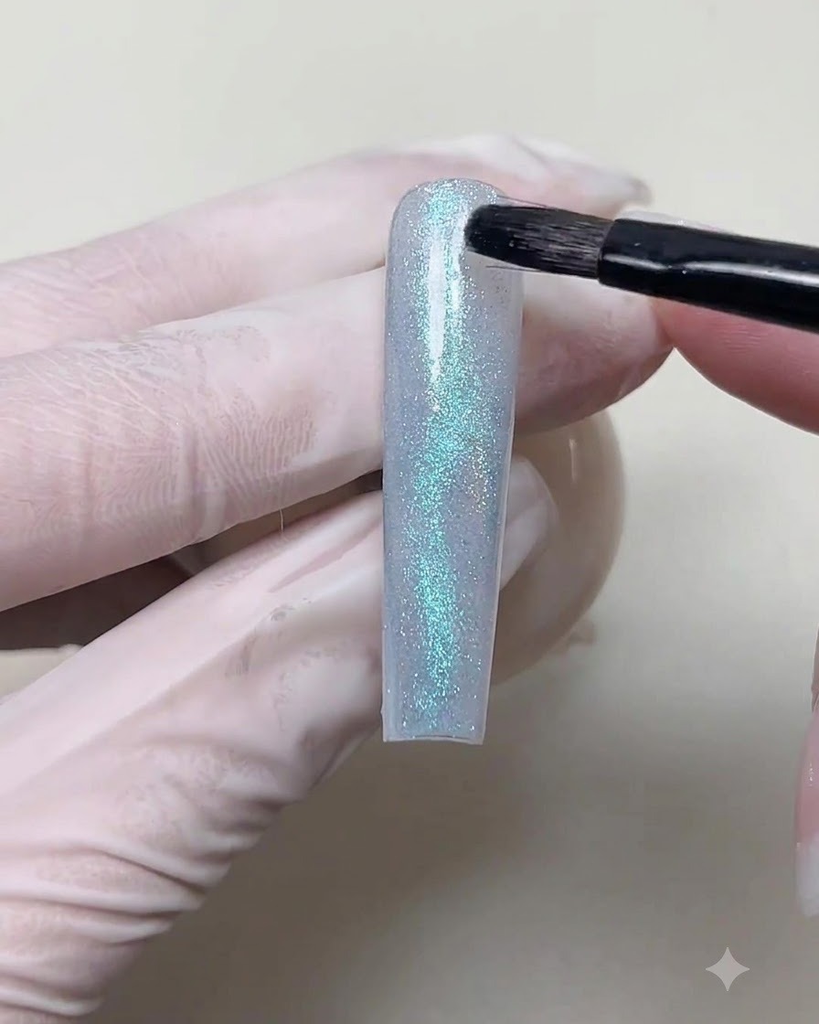 Un pinceau fin de détail déposant un petit point de gel magnétique bleu sur un design cat-eye ondulé.
