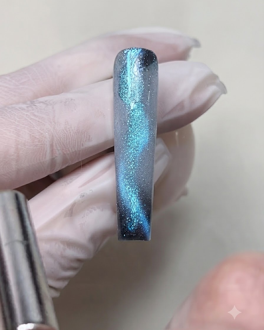 Un aimant cylindrique tenu près du bord dun ongle, attirant le reflet de taches de gel bleu fraîchement ajoutées en une ligne lumineuse.