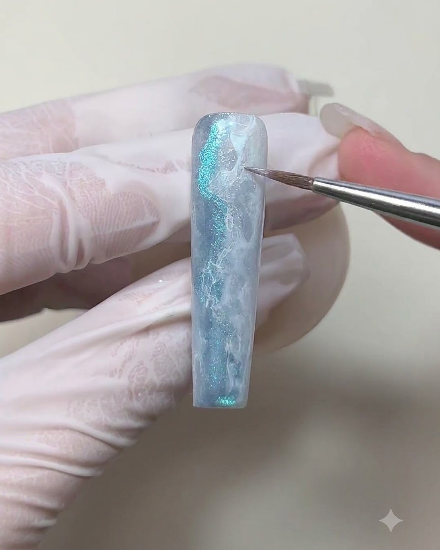 Gros plan dun pinceau liner dessinant de fines lignes blanches sur une surface dongle texturée bleue et blanche.