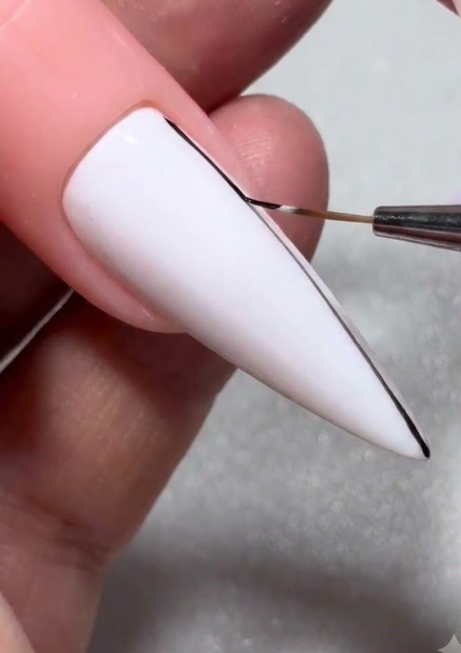 Un gros plan détaillé dun pinceau fin pour nail art dessinant une fine ligne noire sur un ongle en gel blanc.