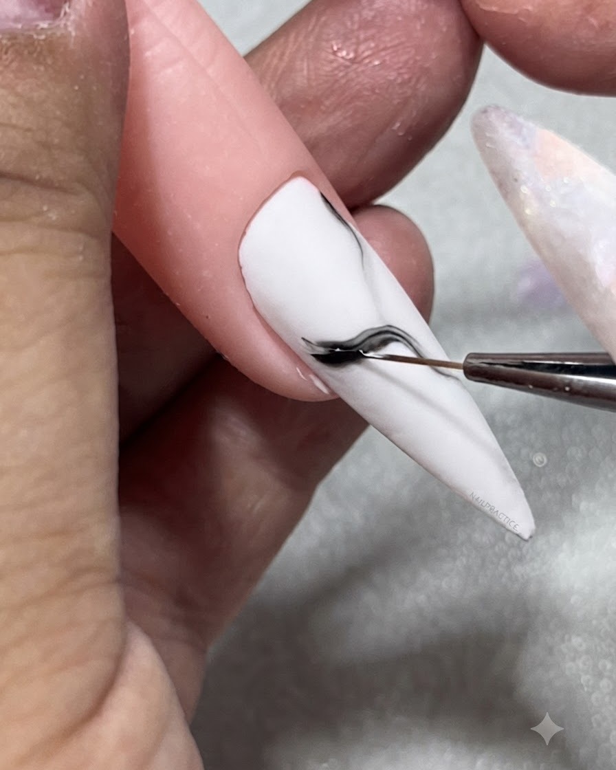 Gros plan dun pinceau liner fin prolongeant une veine de marbre noire vers la zone des cuticules sur un ongle blanc.