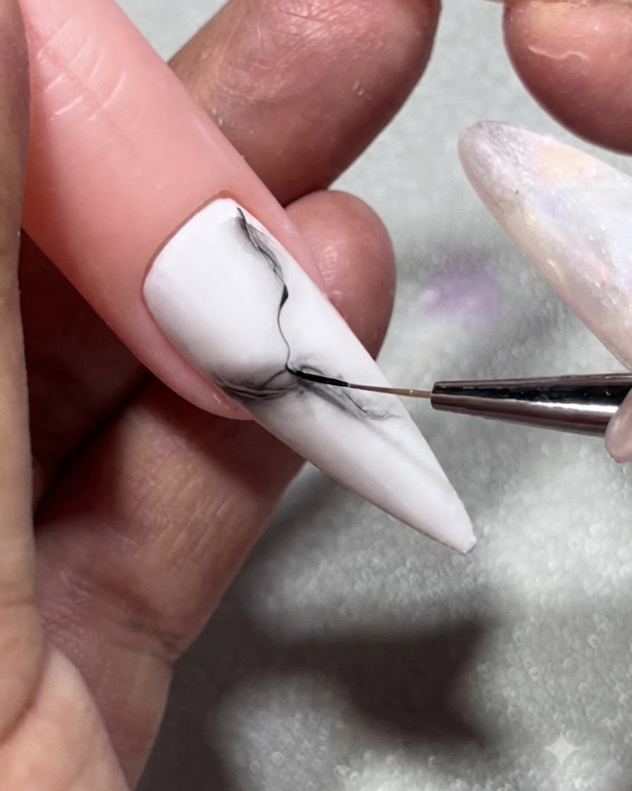 Un pinceau liner pour ongles peignant des détails de veines noires nettes et fines sur un fond en gel marbré noir et blanc flouté.