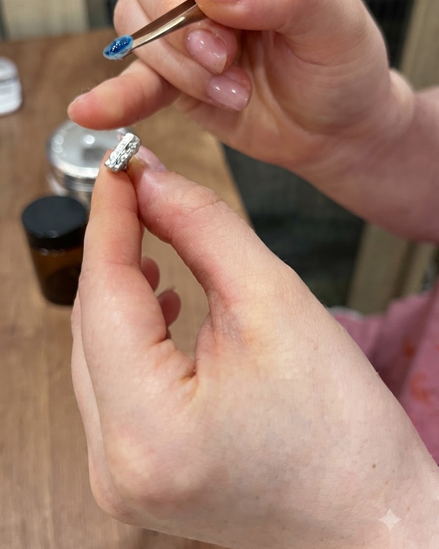 Gros plan dune pince de précision soulevant une petite gemme 3D bleue dun support à ongles magnétique.