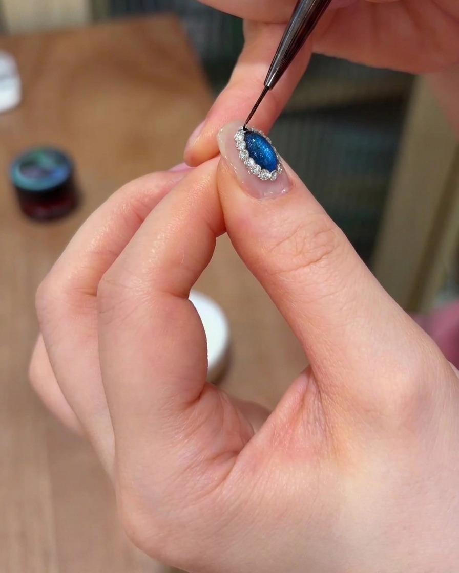 Un pinceau fin liner appliquant de la colle dans les espaces entre les cristaux sur un ongle.
