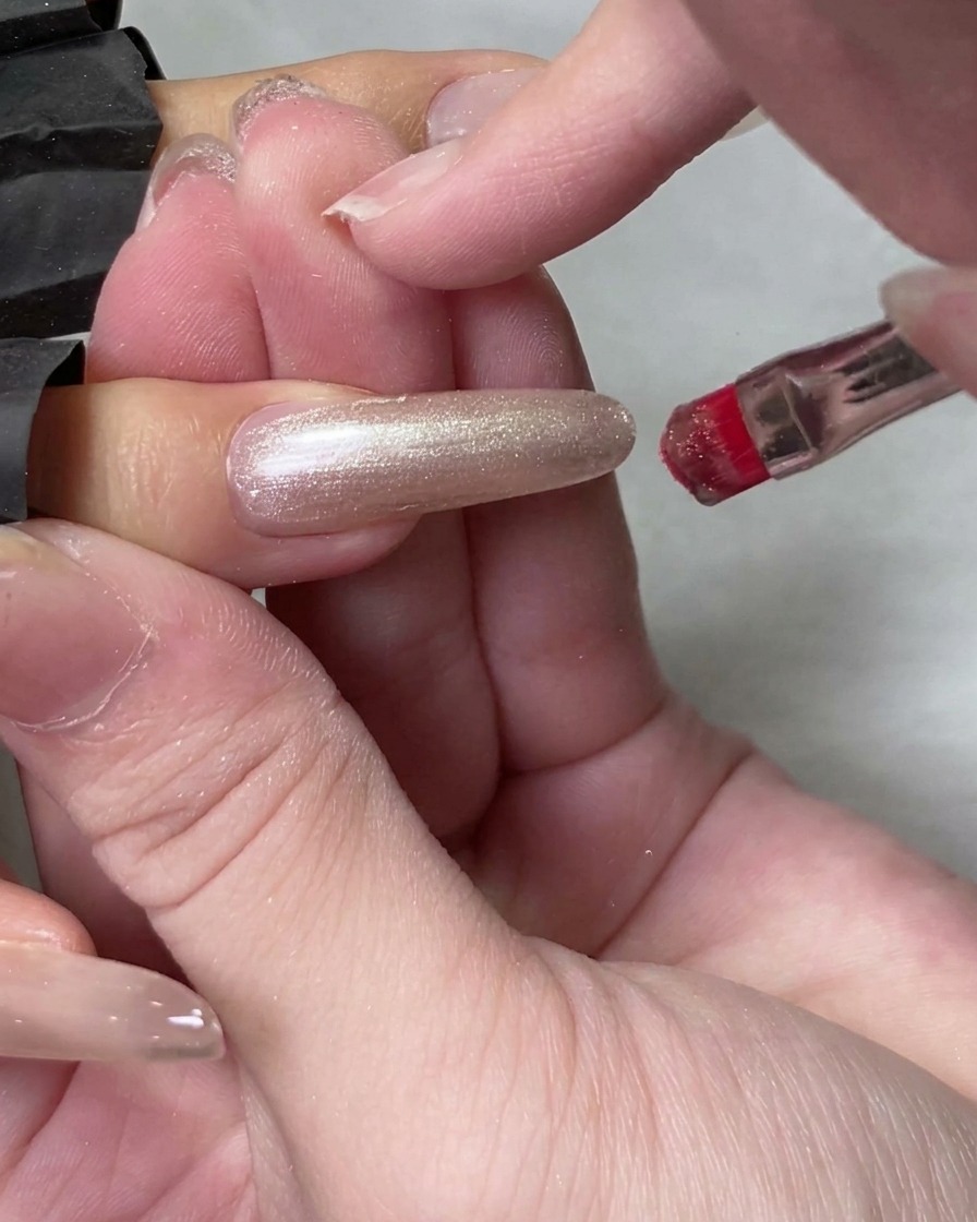 Un pinceau de flacon appliquant du gel cat eye translucide sur un long ongle naturel.